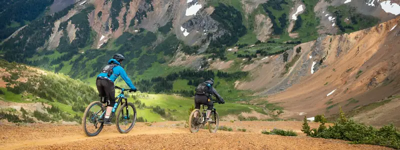 Two riders on a dirt road below rugged mountains