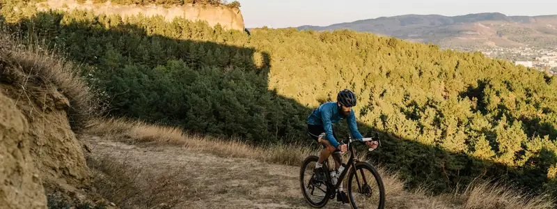 Cyclist riding a dirt trail on a sunny hillside